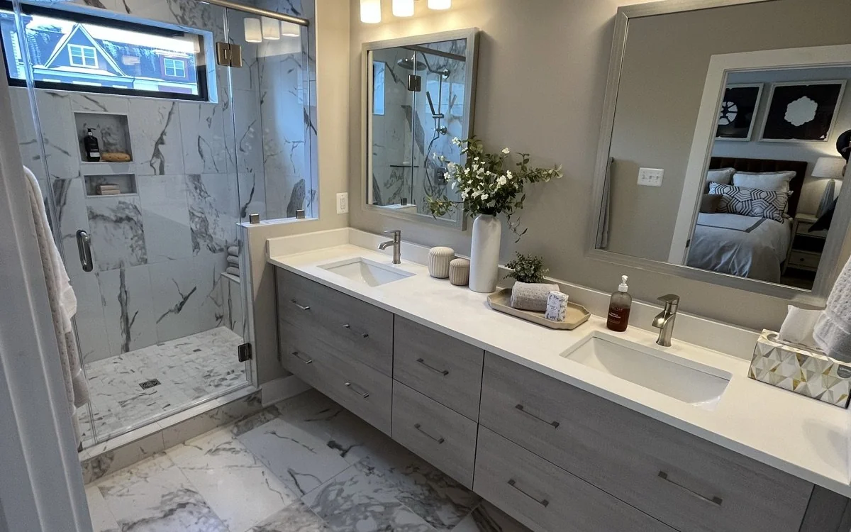 Completed bathroom remodel with a double vanity, marble-look shower, and coordinated tile flooring