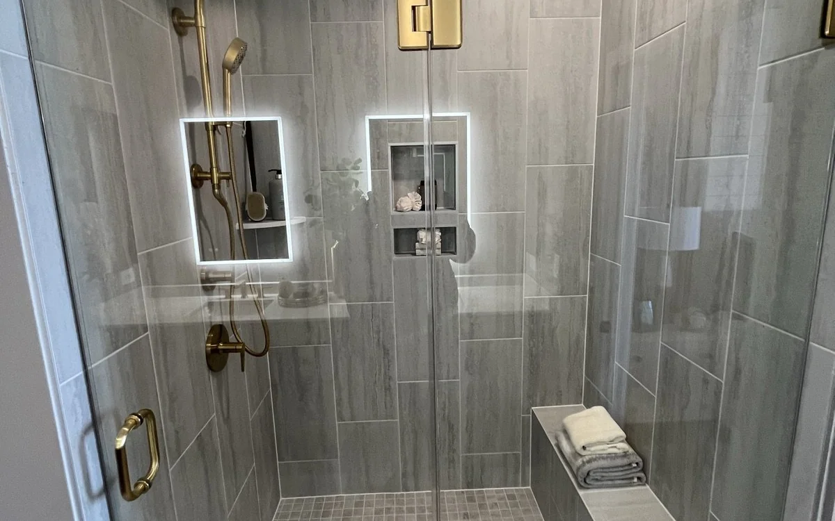 Custom tiled walk-in shower with glass enclosure, recessed niches, and brushed brass fixtures
