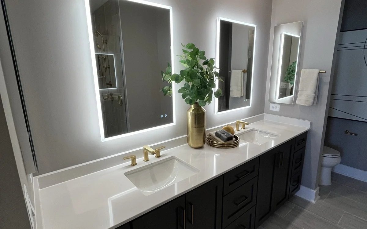Double bathroom vanity with illuminated mirrors, dark cabinetry, and quartz countertop