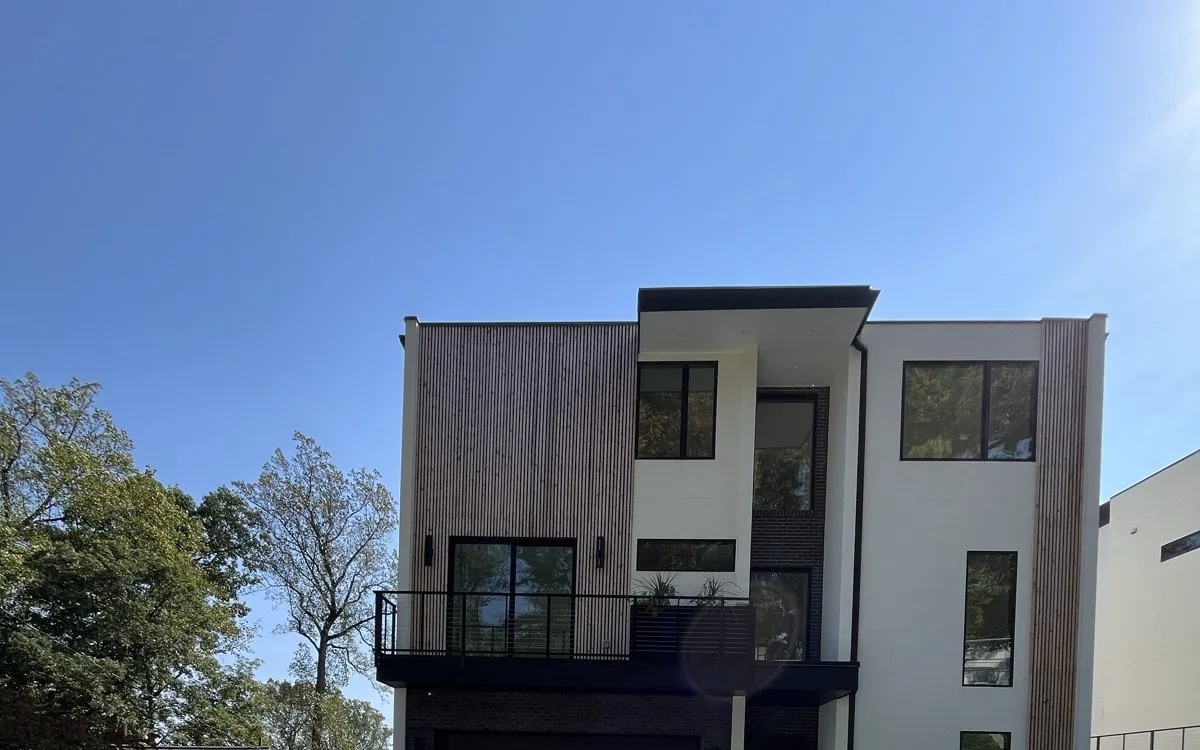 Modern home exterior with white stucco, vertical wood slat accents, large black-framed windows, and a second-floor balcony in a DMV neighborhood
