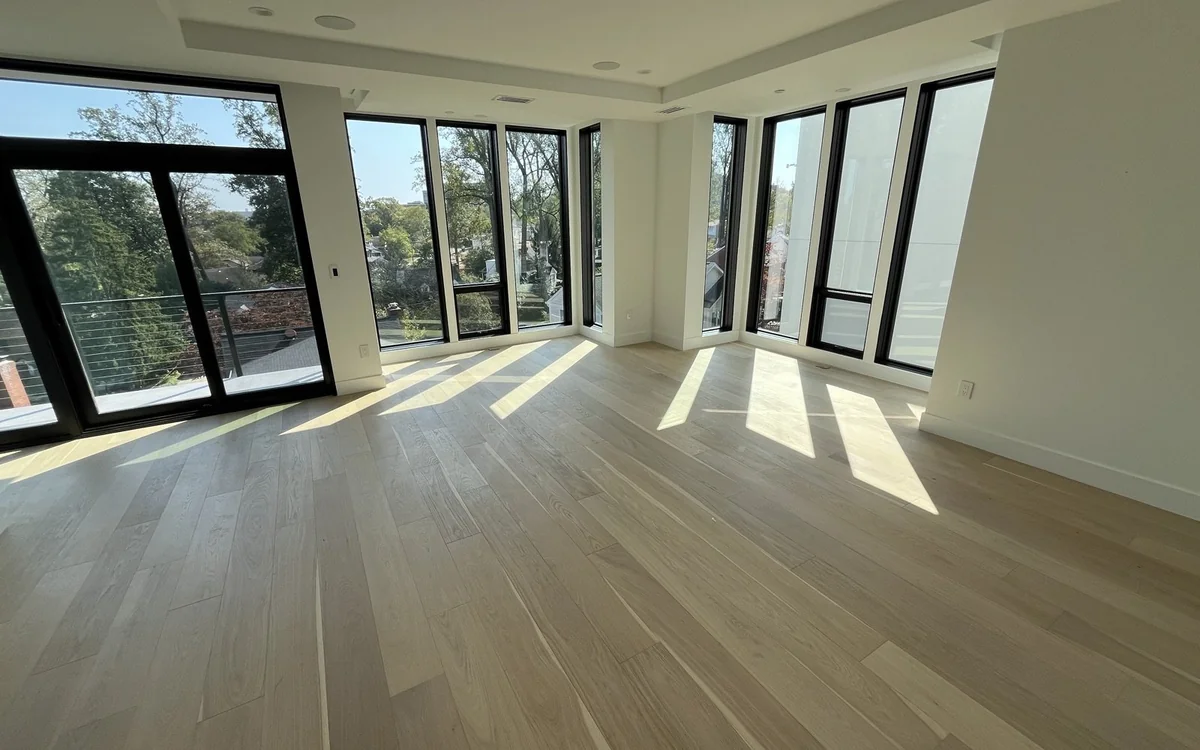 Bright renovated room with wide-plank wood flooring and floor-to-ceiling windows