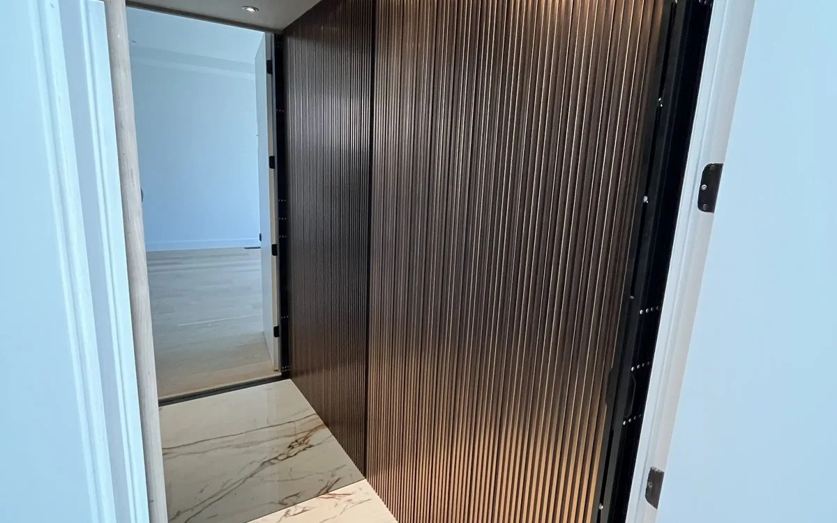Interior of a residential elevator cab with fluted walnut wood panel walls, marble tile flooring, and recessed ceiling lighting