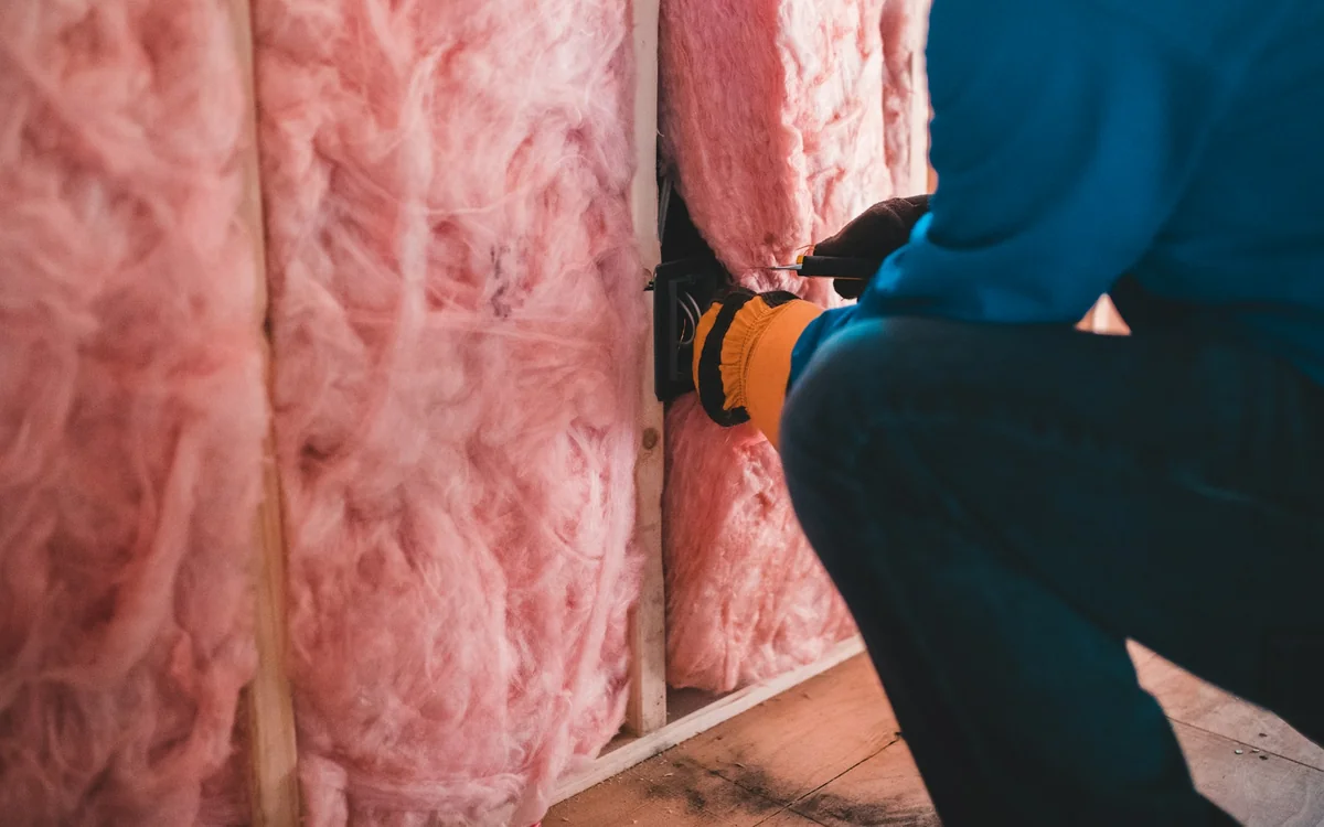 Contractor working beside fiberglass wall insulation before drywall installation