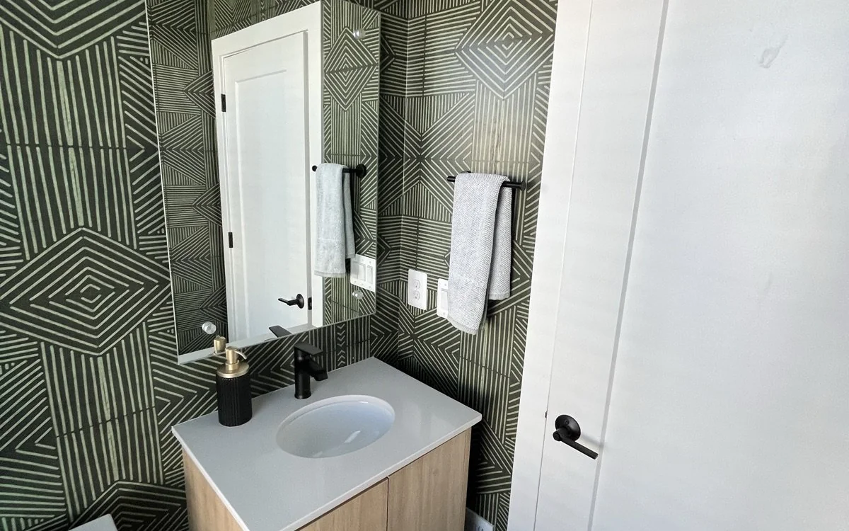 Powder room with bold geometric wall tile, warm wood vanity, and matte black fixtures