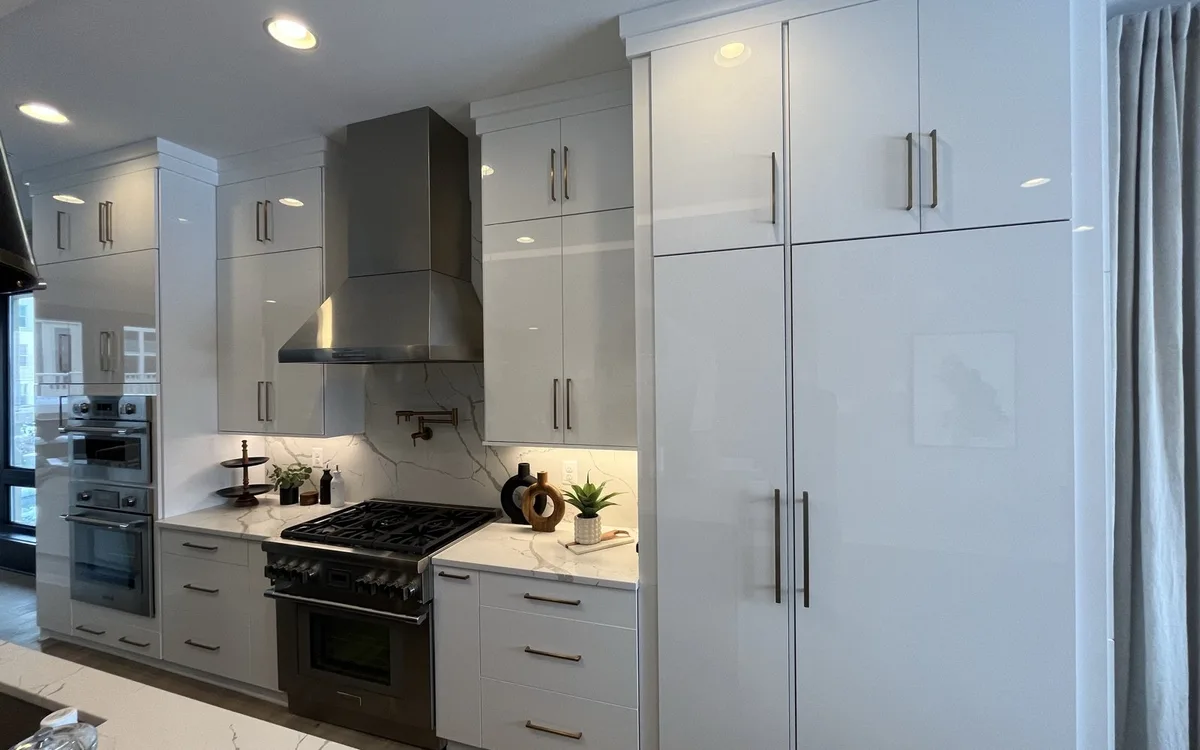 Modern kitchen with high-gloss white slab cabinetry, calacatta quartz countertops, stainless range hood, dark stainless professional gas range, double wall oven, and pot filler