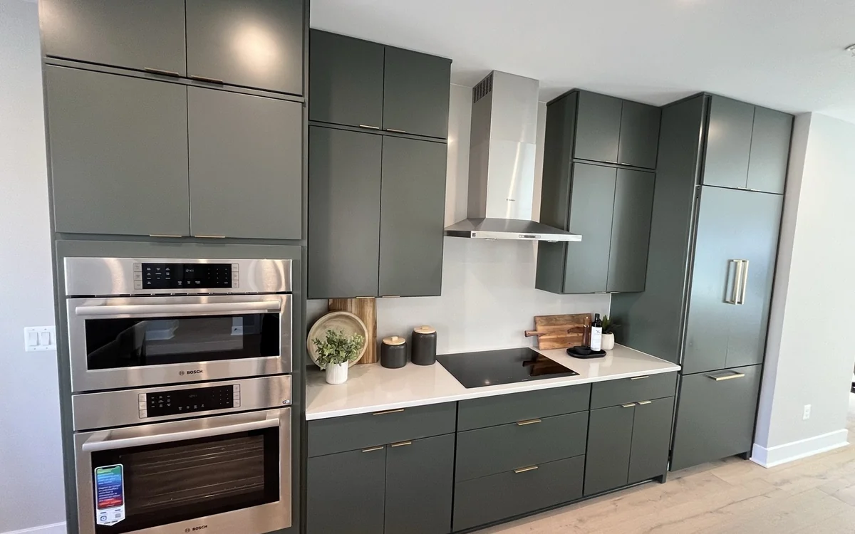 Renovated kitchen with sage green cabinets, integrated appliances, and brass hardware