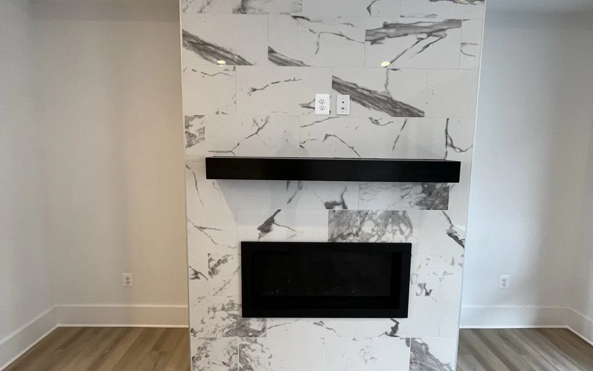 Floor-to-ceiling fireplace surround with large-format calacatta marble-look porcelain tile, recessed linear gas fireplace insert, floating black steel mantel shelf, and recessed spotlights in a renovated living room