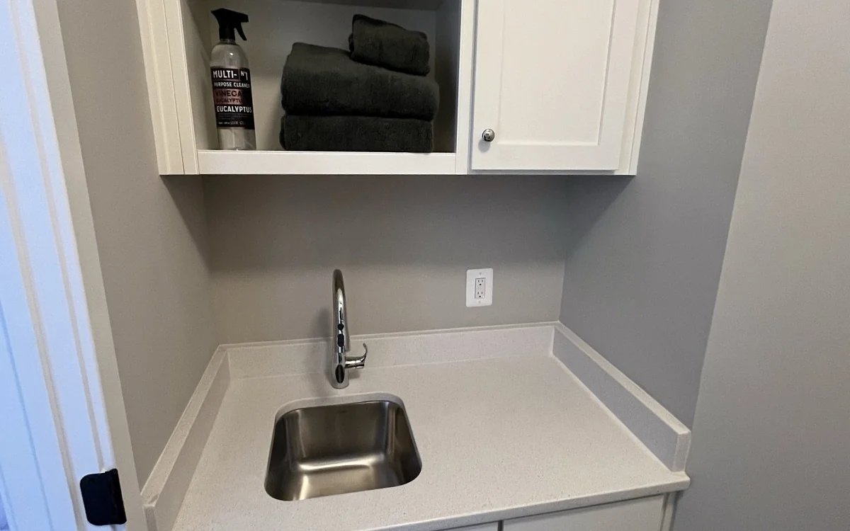 Compact utility room with base cabinets, worktop, and deep sink for laundry and cleanup
