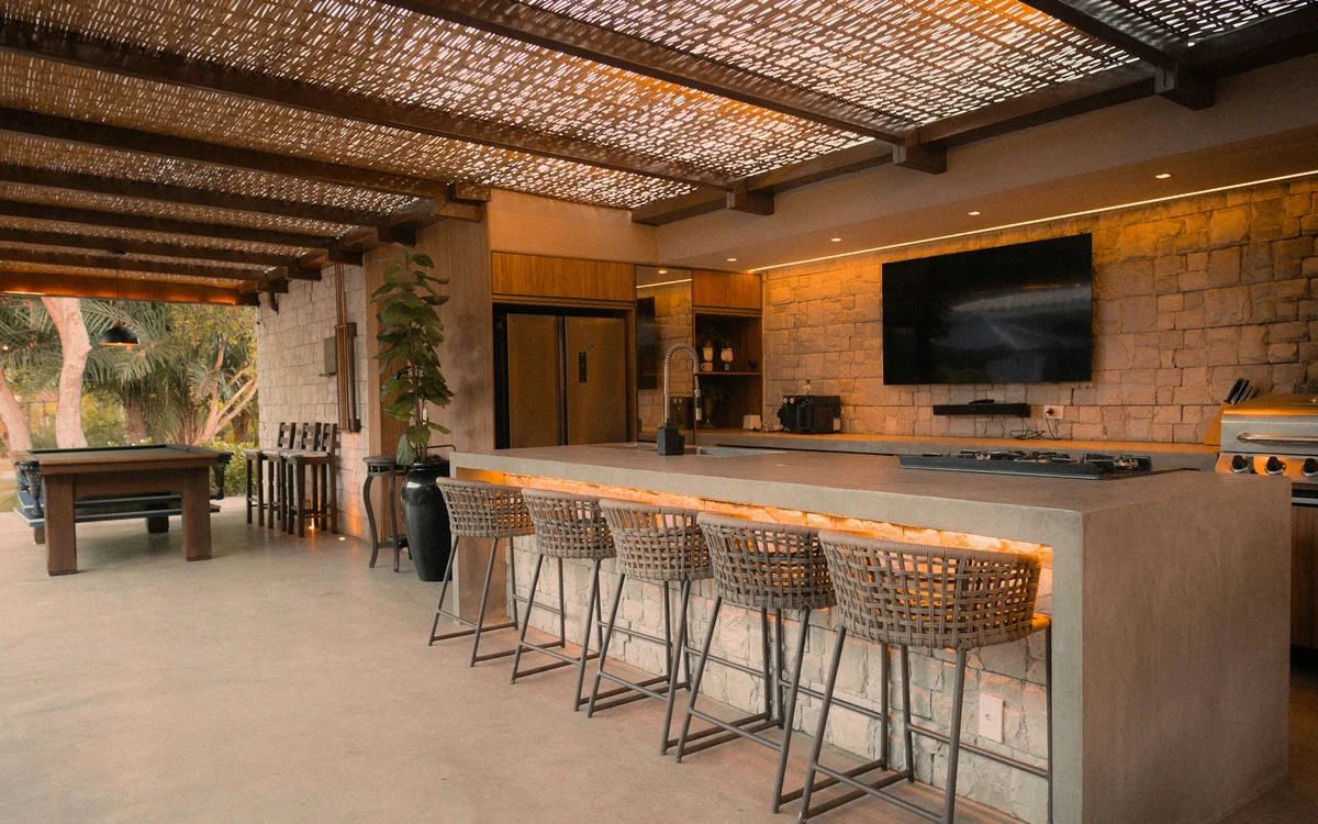 Modern covered outdoor kitchen with built-in grill, island, bar seating, and weather-resistant finishes
