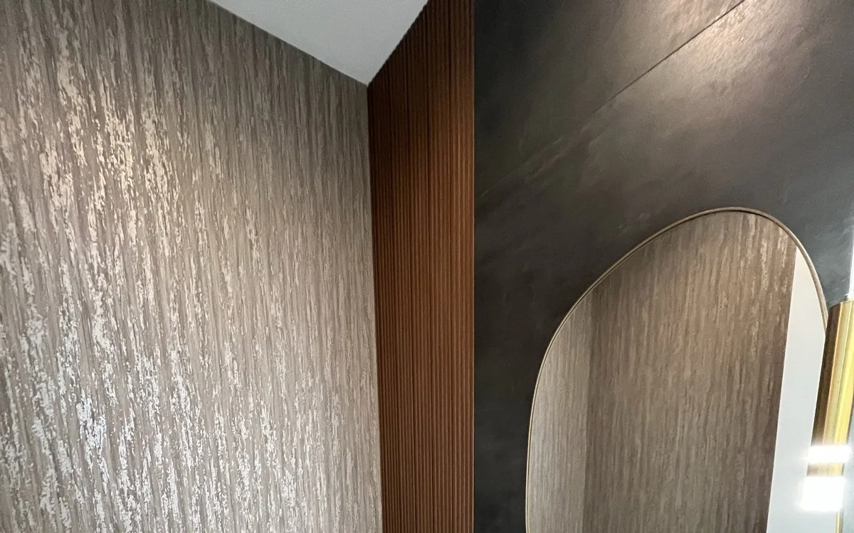 Powder room with textured metallic wall finish, dramatic veined marble floor tile, fluted walnut accent panel, and organic-shaped mirror with gold frame
