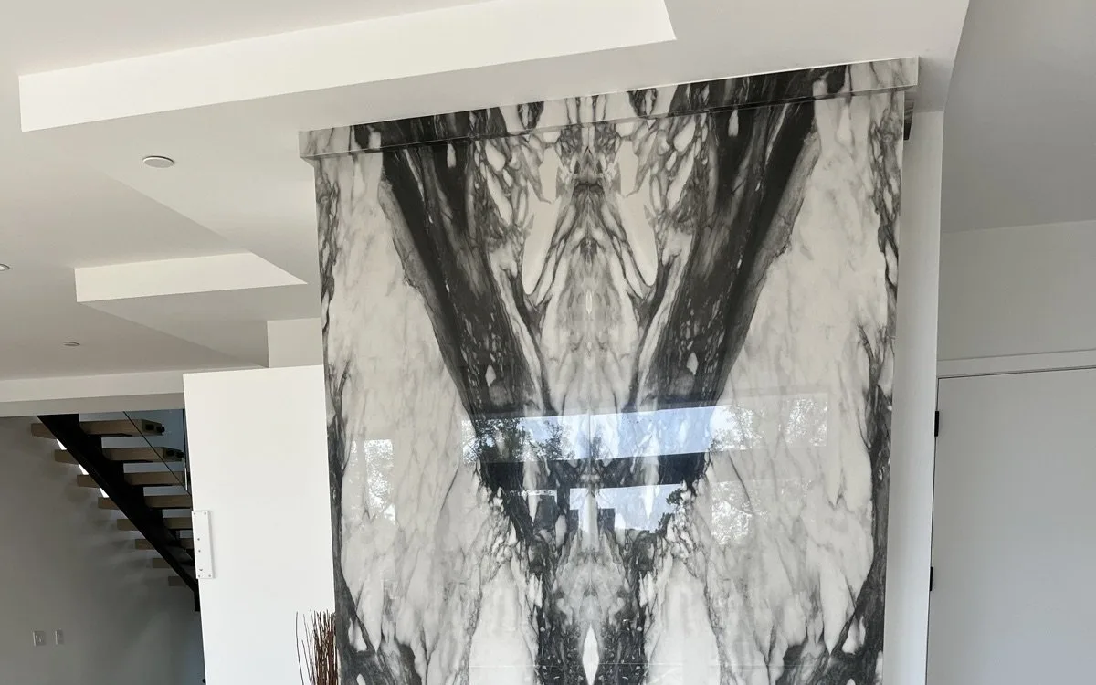 Dramatic bookmatched marble slab feature wall with a wide linear gas fireplace insert and dark marble base in a contemporary living space
